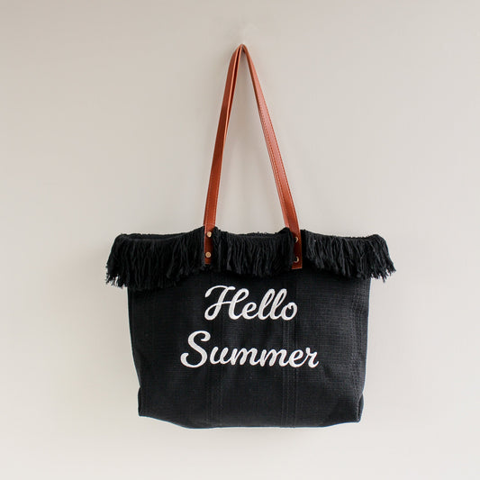 Black tote bag with brown leather handles and fringe trim, featuring white embroidered “Hello Summer” text — a stylish and playful accessory perfect for summer!