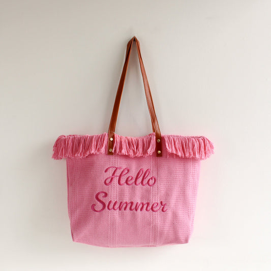 Pink tote bag with brown leather handles and fringe trim, featuring pink embroidered “Hello Summer” text — a stylish and playful accessory perfect for summer!